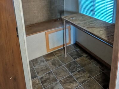 Interior view of a small kitchen with wooden cabinets, a window with blinds, and a countertop.