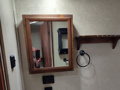 A bathroom vanity with a mirror, towel ring, and small shelf on a beige wall.