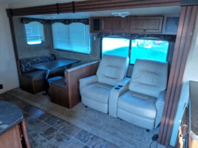 Comfortable living room inside a recreational vehicle with beige recliners and a dining area.