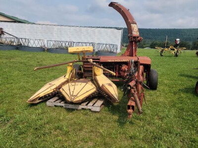 Used agricultural mower with yellow cutting deck and red attachment arm on grassy field.