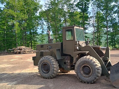 All-Terrain Loader with front bucket attachment, parked outdoors in a wooded area.