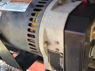 Alternator for agricultural equipment, possibly a tractor or similar machinery, with warning labels and ventilation slots.