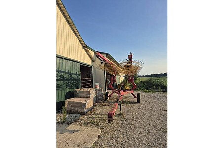 Hay rake attached to a red tractor, used for agricultural hay collection, outdoors on a farm in the late afternoon.