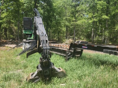 Excavator with a long arm and bucket attachment on grassy field, surrounded by trees.