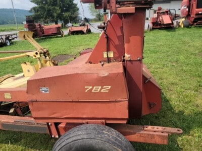 Red New Holland 782 wood chipper with large wheel and extended chute in grassy field.