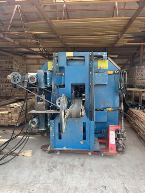 Industrial metalworking machine in a warehouse, blue color, with rollers and control panels.
