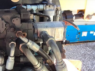 The image shows a close-up of a hydraulic system with various hoses and metal components, likely part of heavy machinery or c.