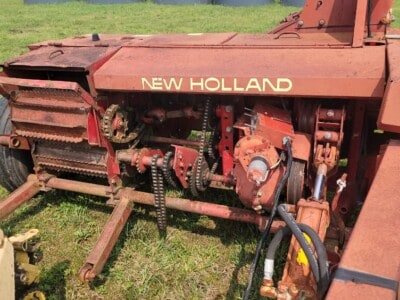Old New Holland tractor with visible tracks and mechanical parts, red paint, and signs of wear.