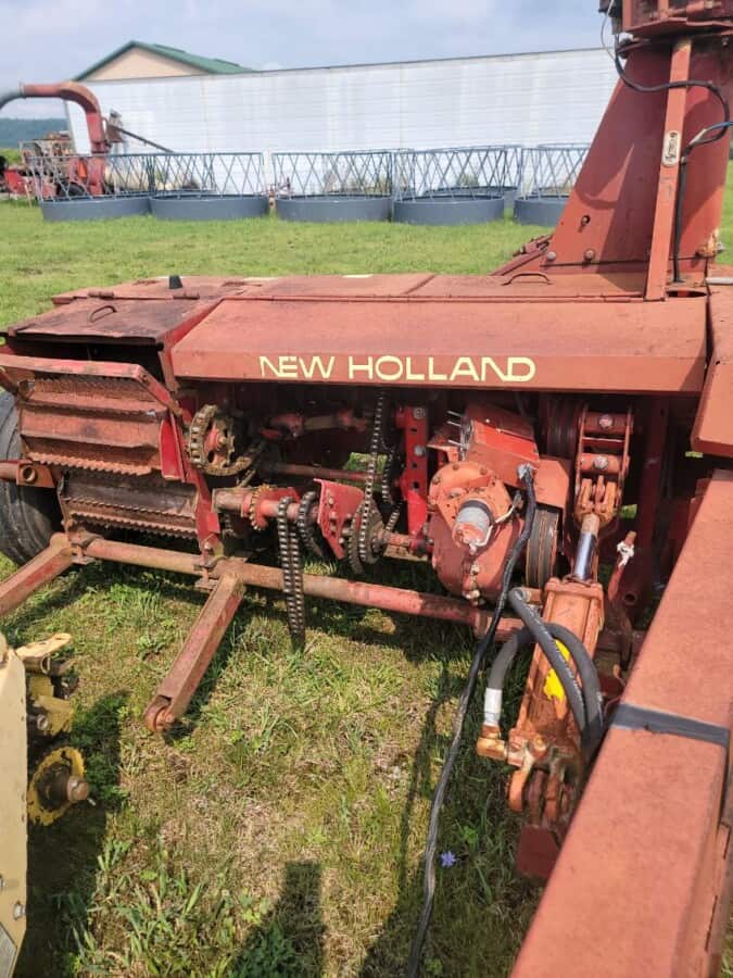 Old New Holland tractor with visible tracks and mechanical parts, red paint, and signs of wear.