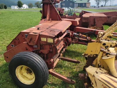 Red New Holland 782 forage harvester with yellow cutting head on green field.