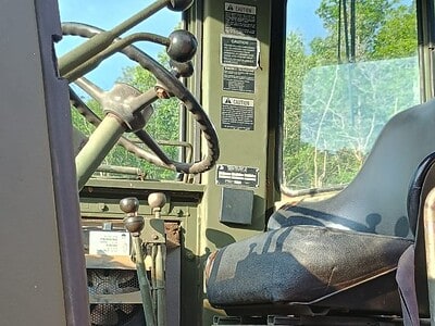 Interior view of a vintage tractor cab with steering wheel and control levers, no visible year or model.