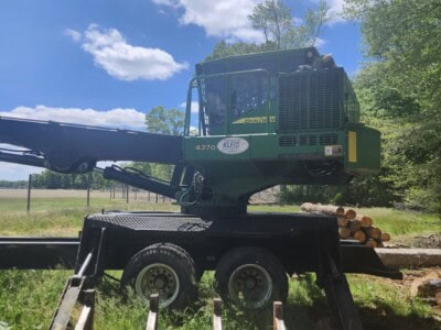 Green John Deere 4370 logging excavator with extended arm and logs, outdoors on a sunny day.