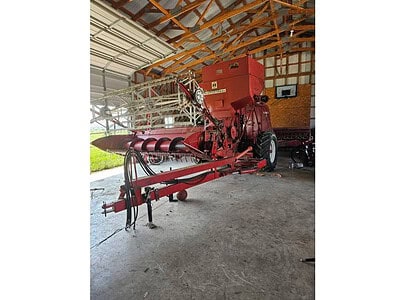 John Deere 7000 Series corn harvester with red body and large tires, stored inside a barn with wooden roof structure.