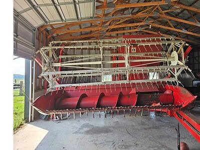 Red and white agricultural combine harvester stored in a barn with wooden roof structure.
