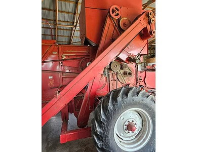 Red vintage tractor with large rear wheel inside a barn, no visible year or model.
