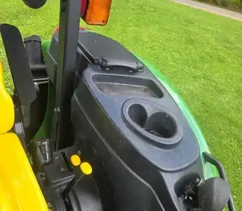 Green and black tractor dashboard with cup holders and control levers, outdoors on grass.