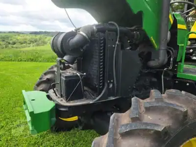 Close-up of green John Deere 5425 tractor engine and front wheel on grassy field.