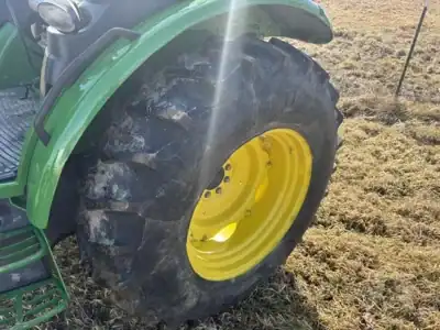 Large green tractor tire with yellow rim on a grassy field.