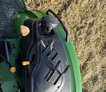 Green John Deere tractor dashboard with steering wheel and control levers in an outdoor field setting.