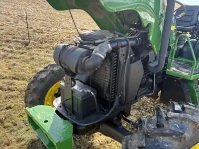 Green John Deere tractor with exposed engine and large rear tire in a field.