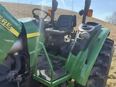 Green John Deere tractor with black seat and large rear tires, parked outdoors on a dirt surface.