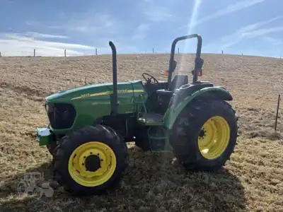 John Deere 5075E tractor from 2020 with large rear tires and a green and yellow color scheme, parked on a grassy field under.