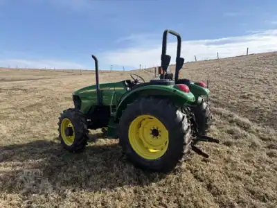 Green John Deere tractor with yellow wheels on a grassy field under a blue sky.