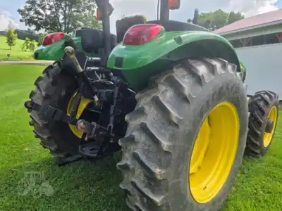 Green John Deere tractor with large rear tires and enclosed cab on grassy field.
