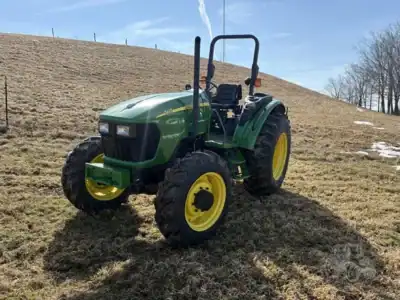 Green John Deere compact tractor with yellow wheels on grassy field under blue sky.