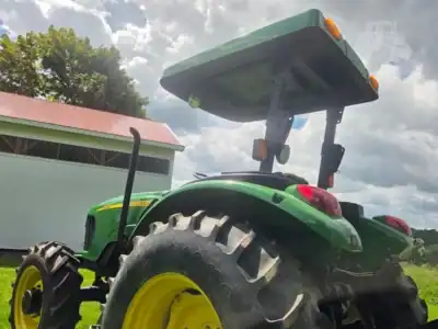Green John Deere tractor with yellow wheels and canopy, large rear tires, outdoor setting.