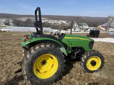 Green John Deere tractor with yellow wheels, model unspecified, on a grassy field with a rural background.