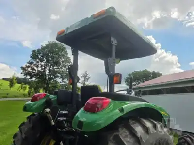 Green tractor with canopy and large rear tires, outdoor setting with trees and cloudy sky.