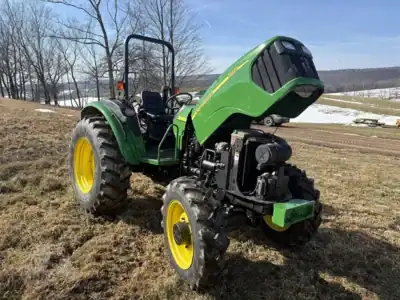 Green John Deere 2023 compact utility tractor with front loader attachment on a farm field.