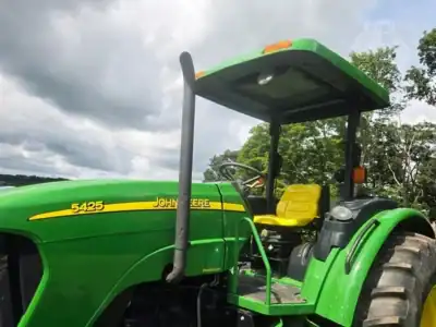 2007 John Deere 5425 tractor with green body and yellow seat under cloudy sky.