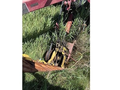 Farm equipment attachment with red frame and yellow parts, situated in a grassy field.