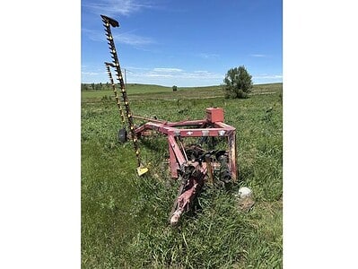 Red agricultural machinery with a tall, black and yellow striped attachment, situated in a grassy field under a blue sky.