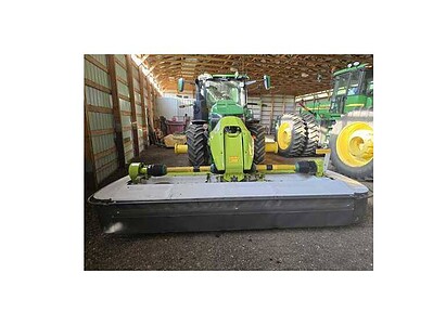 Green John Deere 2020 tractor with mower attachment inside a barn, with other farm equipment nearby.