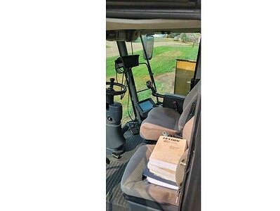 Interior view of a John Deere 5075E tractor showing the seat, controls, and a stack of manuals or documents on the seat.
