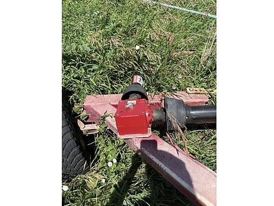 Farm equipment featuring a red hydraulic component and black pipe, situated in a grassy outdoor setting.