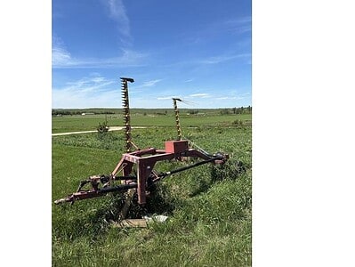 Vintage cultivator for farming, featuring rusted metal tines and frame, set in a green field under a blue sky.