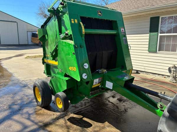 John Deere 458 bale wrapper with green body and black rollers, yellow wheels, and hitch for attachment.