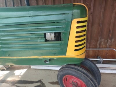 Green Oliver 77 tractor with yellow accents and black tires, parked on concrete surface.