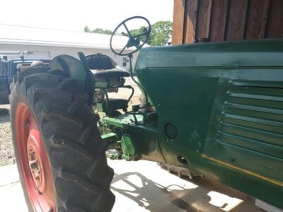 Green Oliver 77 tractor with large rear tires and open operator seat, parked outdoors.