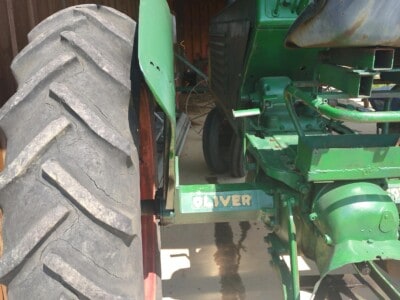 Green Oliver 77 tractor with large rear tire and black steering wheel in a barn.