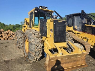 John Deere 6020 forestry tractor with front blade and tracks, yellow and black, on dirt ground.