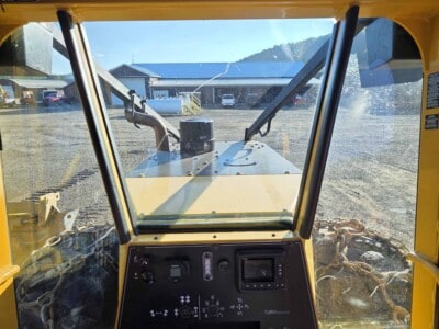 View from inside a yellow construction vehicle cab with controls and large front window.