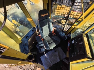 Interior view of a yellow Caterpillar excavator cab with a Tigercat seat and control panel.