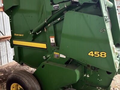 Green John Deere 458 round baler with yellow wheels and black tires, showing hydraulic components and model number.