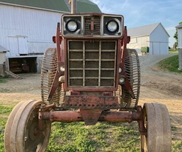Old red farm tractor with tracks and large front wheels, front view, outdoor rural setting.