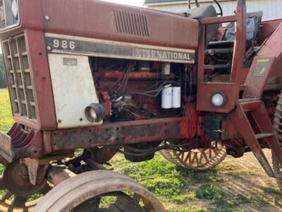 International 986 tractor with visible engine and large rear wheels on a farm.
